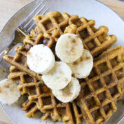 Overhead view of pumpkin waffles on gray plate topped with banana slices, cinnamon sprinkles, and syrup
