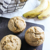 Whole wheat banana bread muffins on cutting board with filled basket behind