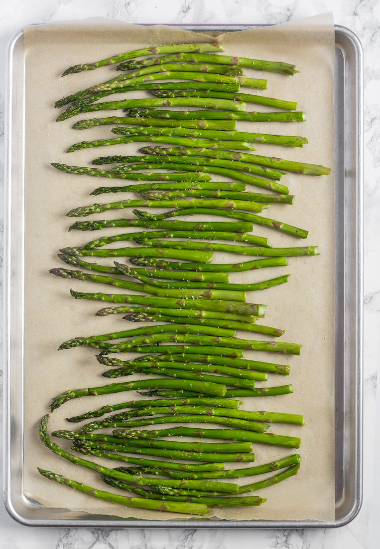 raw asparagus spears on baking sheet