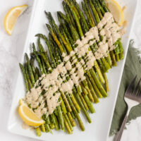 overhead view of roasted asparagus with tahini on white serving plate