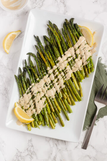 overhead view of roasted asparagus with tahini on white serving plate