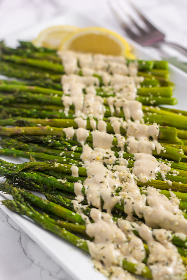 close up side view of roasted asparagus spears drizzled with tahini