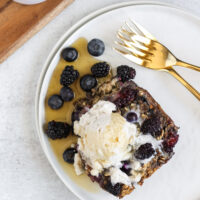 overhead view of a piece of baked berry oatmeal with coconut whipped cream and syrup on top