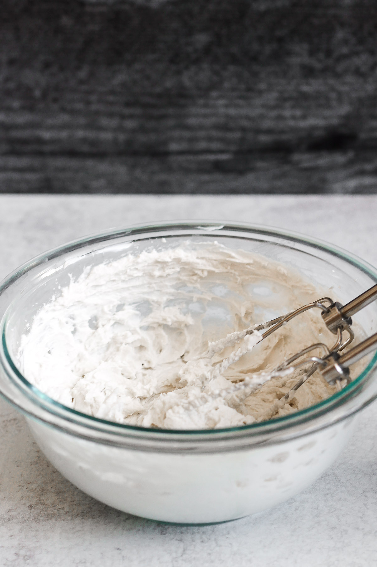 side angle view of coconut whipped cream in glass mixing bowl with electric mixer whisks