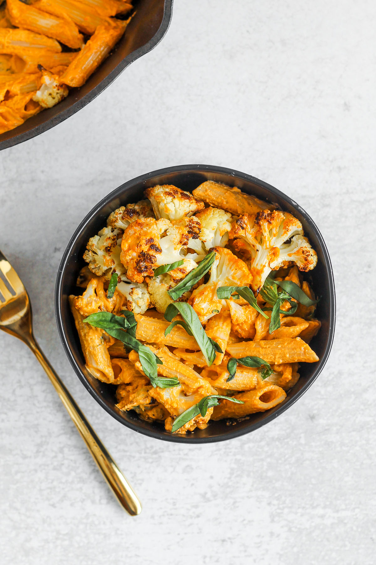 a small black bowl filled with penne pasta tossed with roasted red pepper sauce 