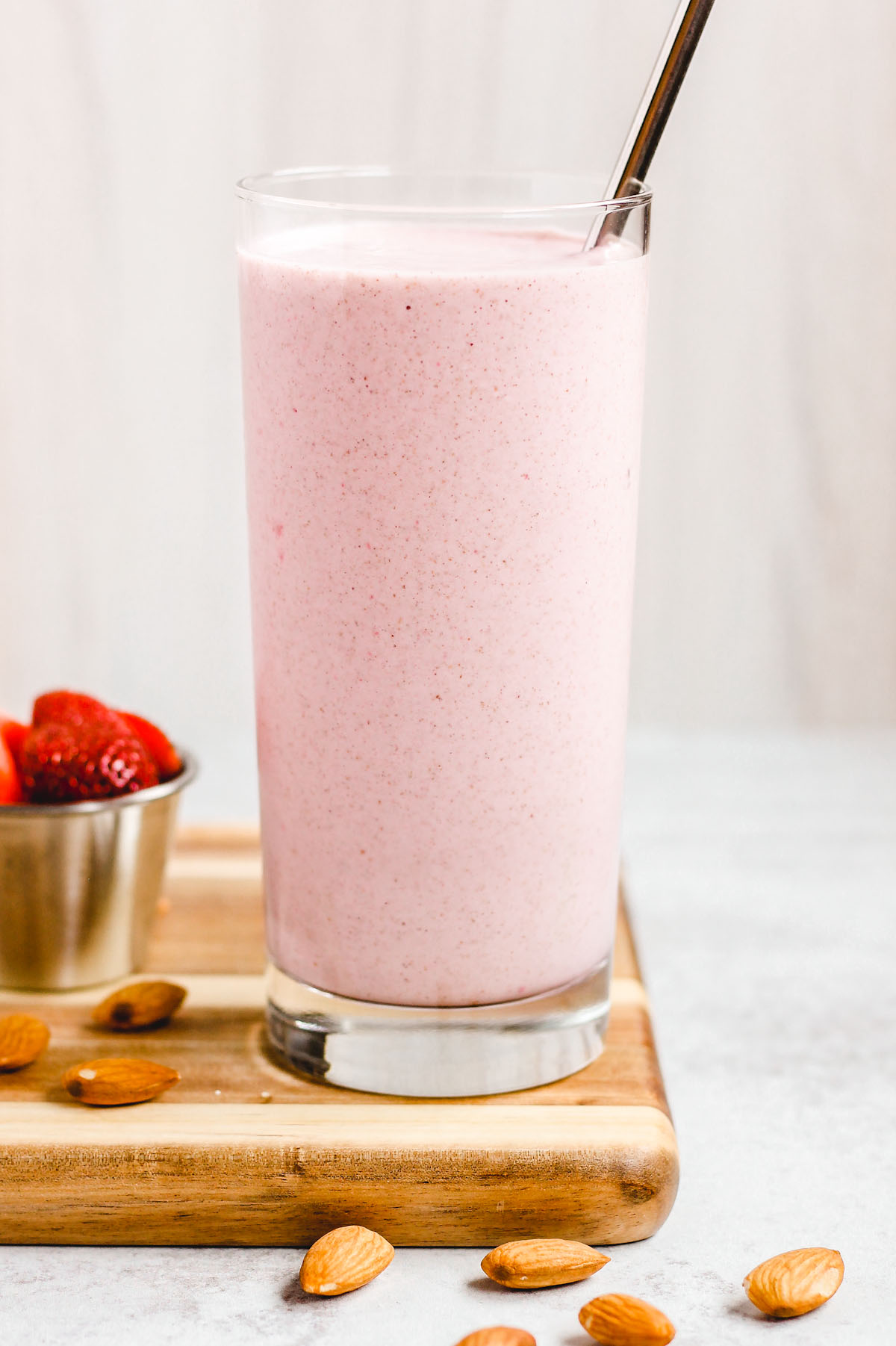 side view of strawberry almond smoothie in a tall glass with stainless steel straw
