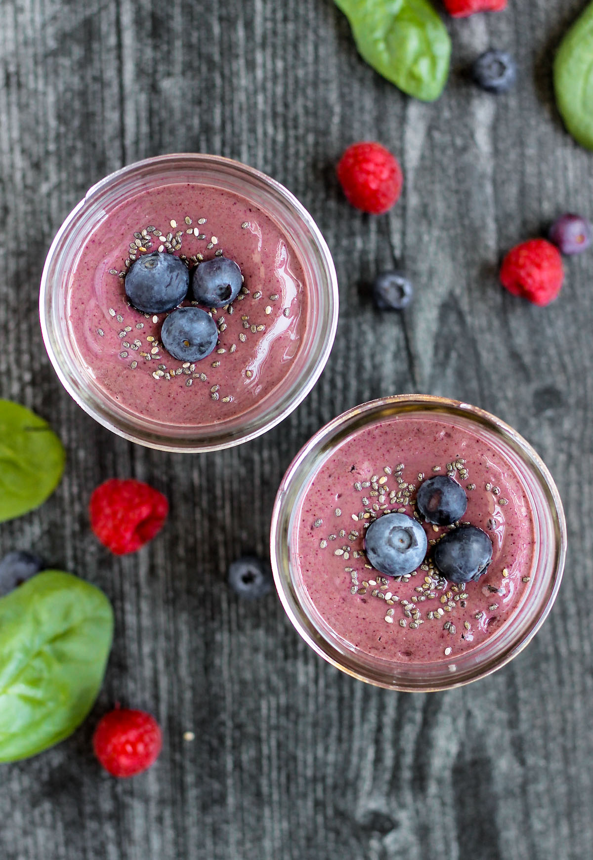 overhead view of two smoothies topped with blueberries with berries and spinach sprinkled on the surface