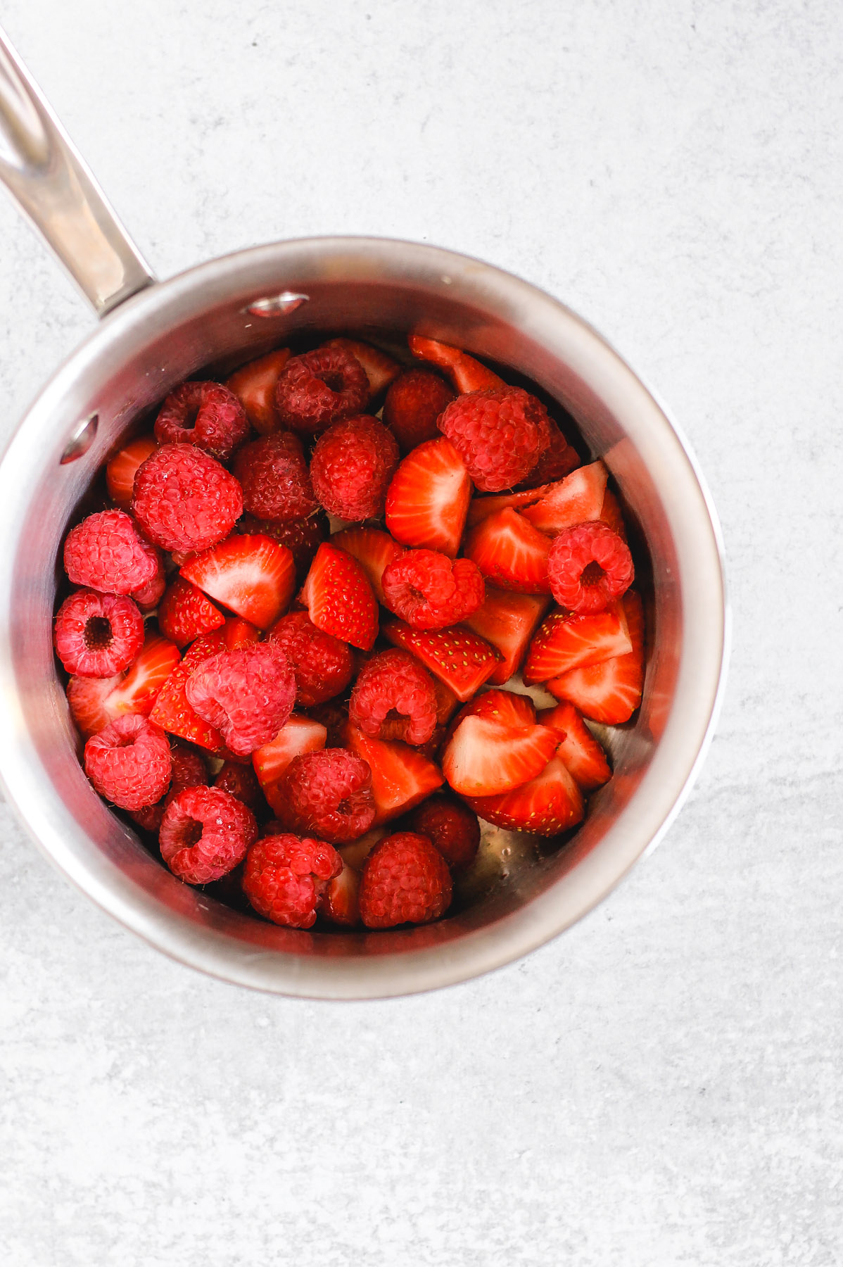 overhead view of sliced strawberries and raspberrries in stainless steal sauce pan