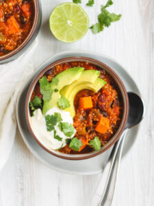 overhead view of two bowls of chili. One on a white plate with spoons resting on the plate.