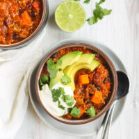 overhead view of two bowls of chili. One on a white plate with spoons resting on the plate.
