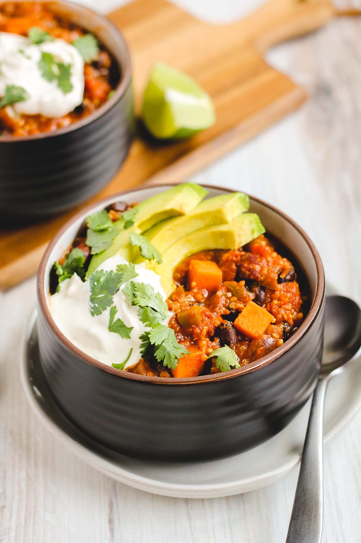 black bowl filled with sweet potato chili topped with sliced avocado, cilantro, and sour cream