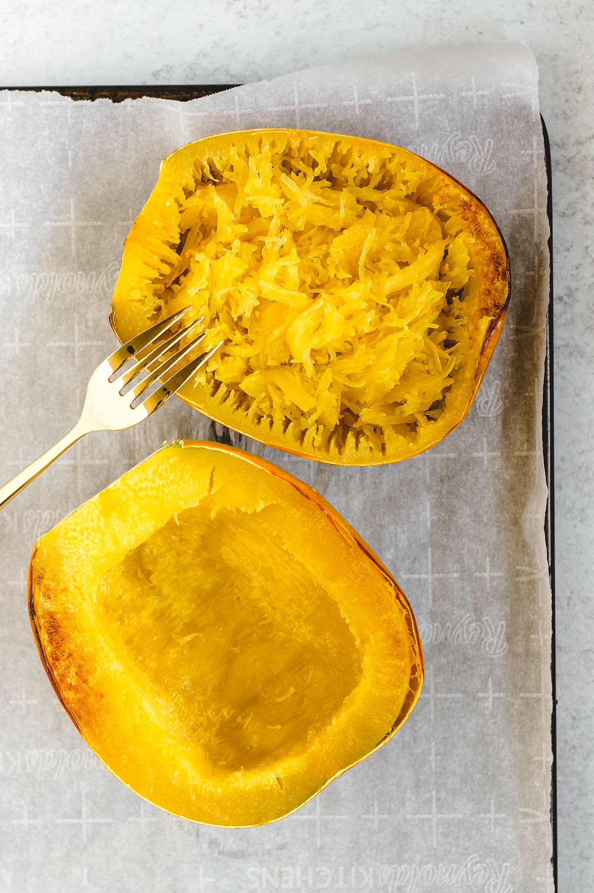 2 roasted spaghetti squash halves - one half has the the squash scraped with a fork showing the spaghetti squash "noodles". 