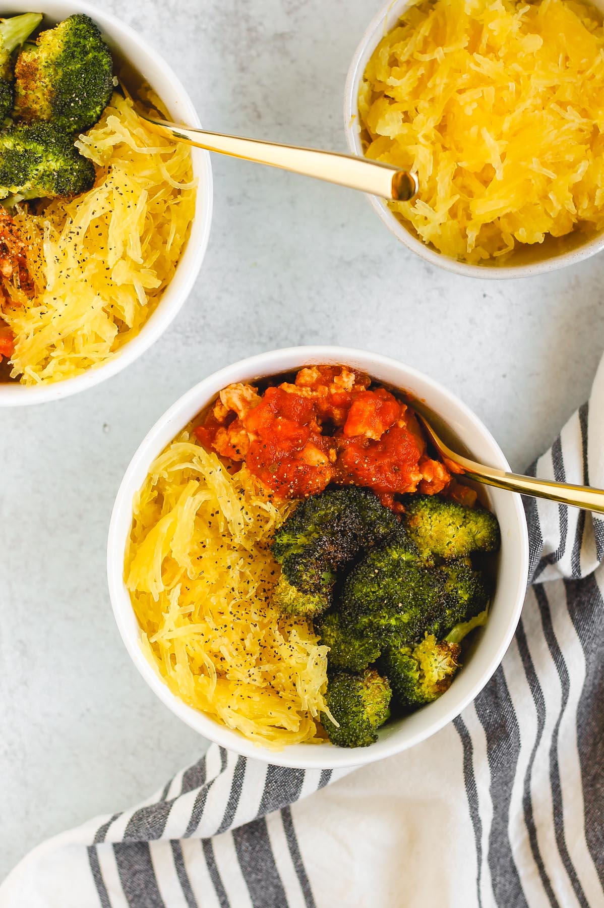 two white bowls with spaghetti squash, roasted broccoli, and turkey marinara sauce in each bowl. 