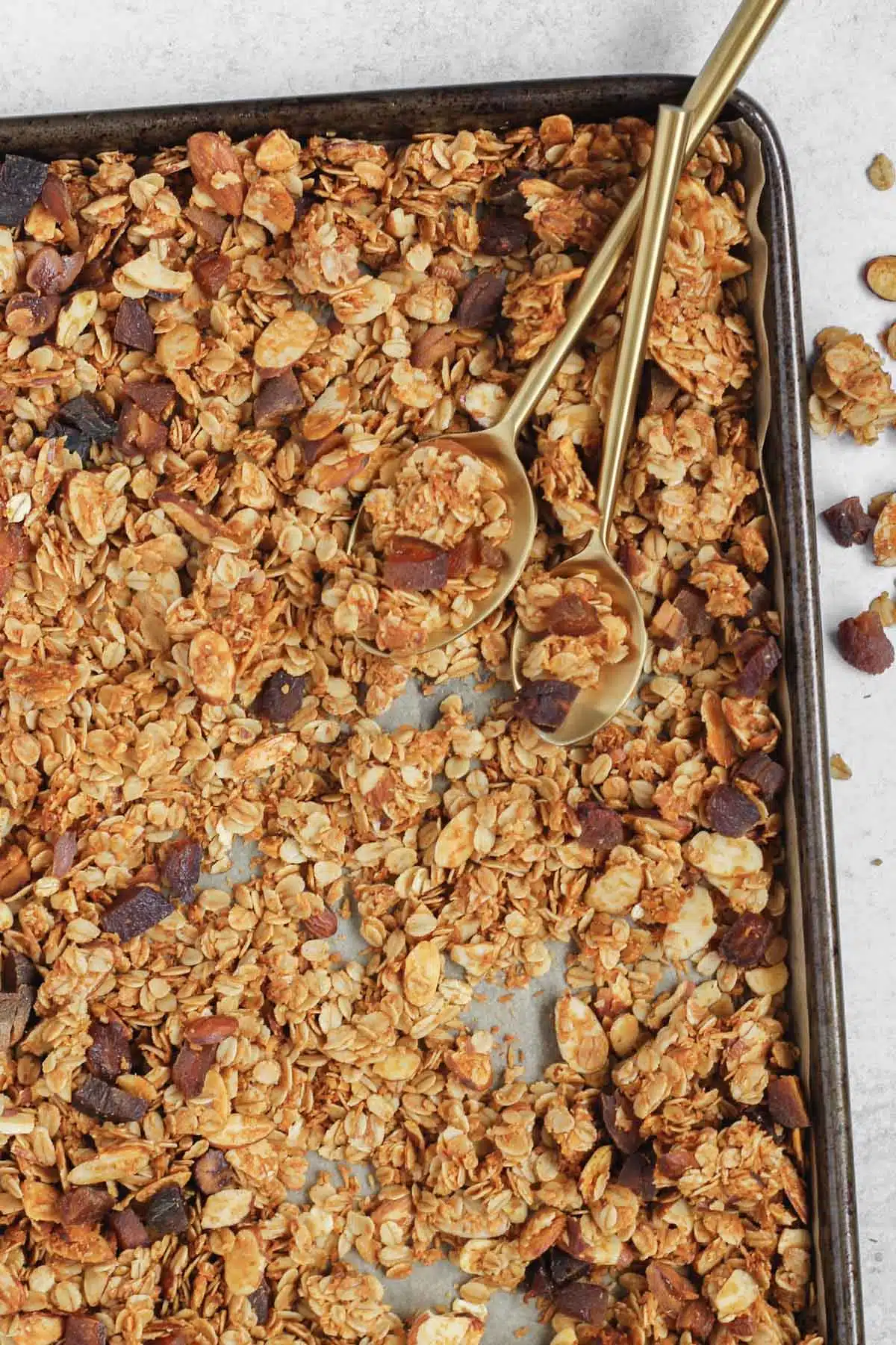 Baked granola on a rimmed baking sheet with two spoons in the granola.