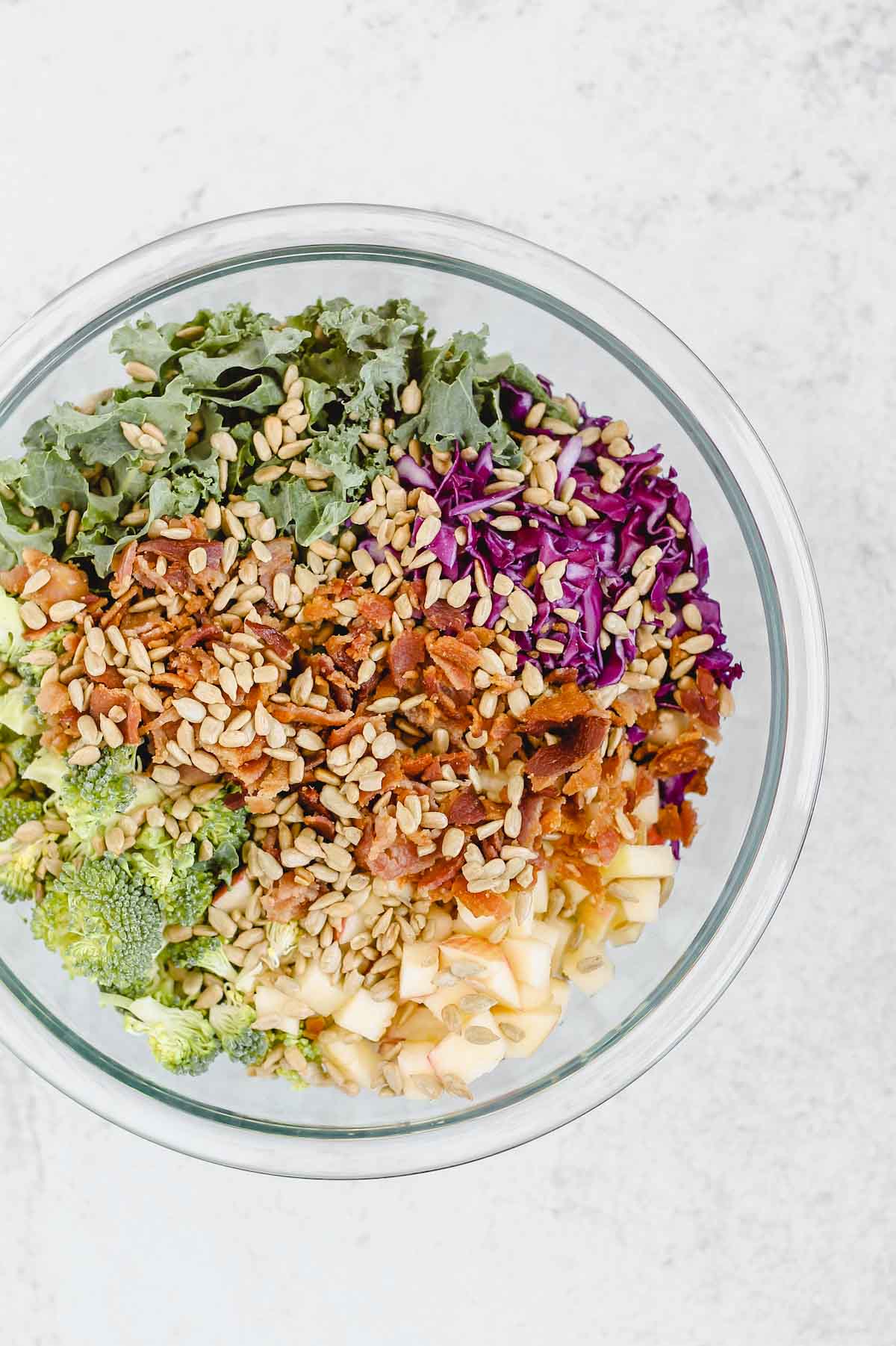 broccoli, kale, bacon, cabbage, apples, sunflower seeds in a glass mixing bowl