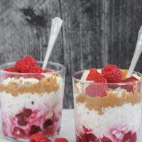 two glass cups filled with overnight oats, raspberries, almond butter, and almonds