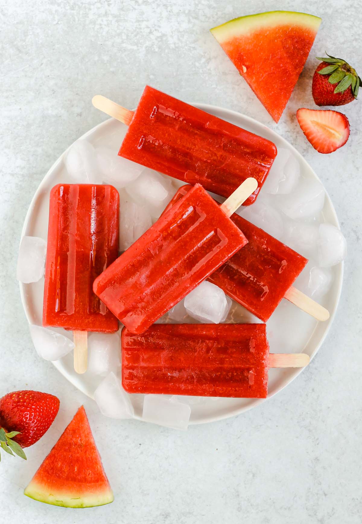 strawberry watermelon popsicles on a round white plate with ice cubes
