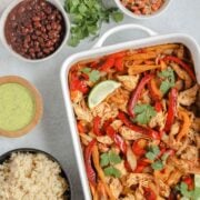 oven baked fajitas in a white baking dish with fajita ingredients in separate bowls around fajita bake