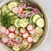 Cucumber radish salad in a serving bowl with red onion and sprigs of fresh dill.