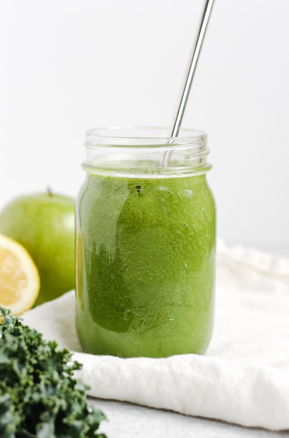 Apple kiwi kale smoothie in a mason jar with a stainless steel straw.