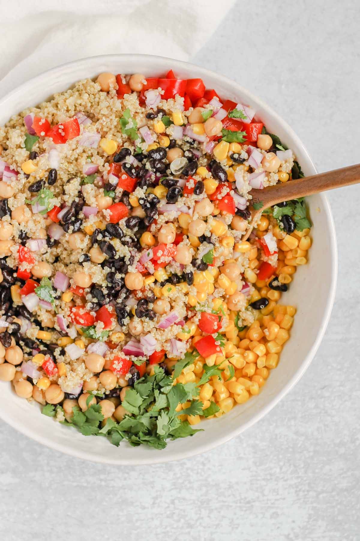 Southwest quinoa salad ingredients mixed together in a large serving bowl with a large wooden spoon in the bowl.
