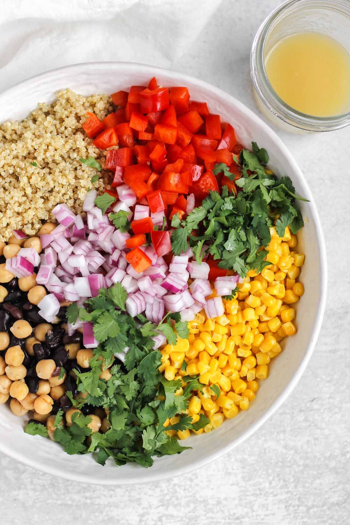 Southwest quinoa salad ingredients, separated in piles, in a large serving bowl with a mason jar of dressing on the side.