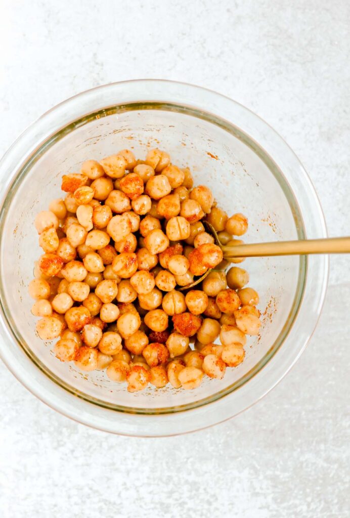 Chickpeas and seasoning mixed together in glass mixing bowl. 