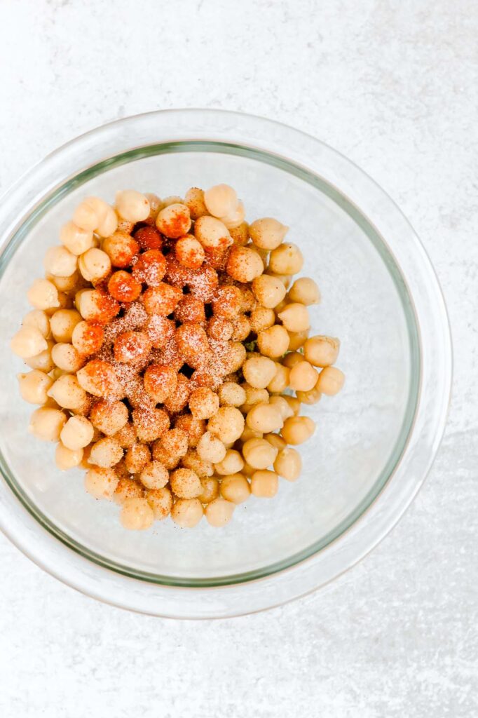 Seasoning sprinkled on chickpeas in a glass mixing bow.