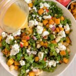 Dressing being poured on kale salad with butternut squash.
