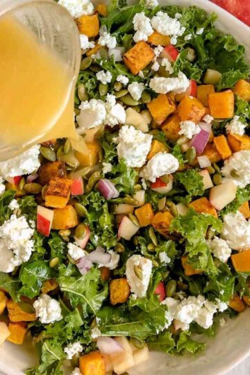 Dressing being poured on kale salad with butternut squash.