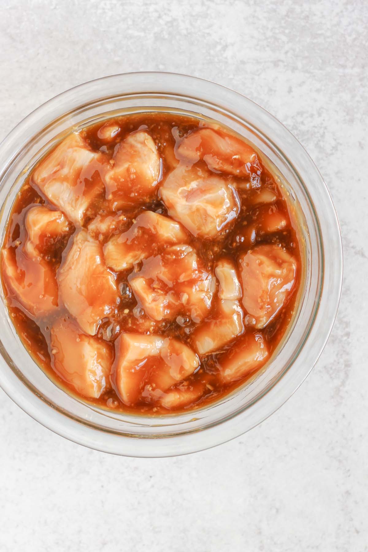 Cut up chicken pieces in a bowl with teriyaki sauce.