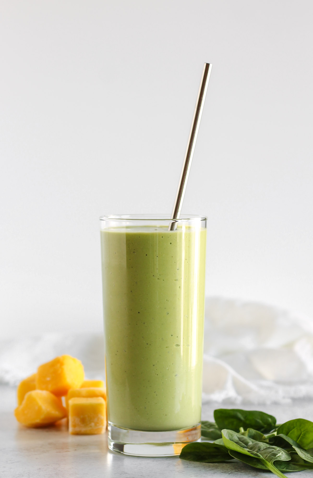 Spinach mango smoothie in a tall glass with a stainless steel straw.