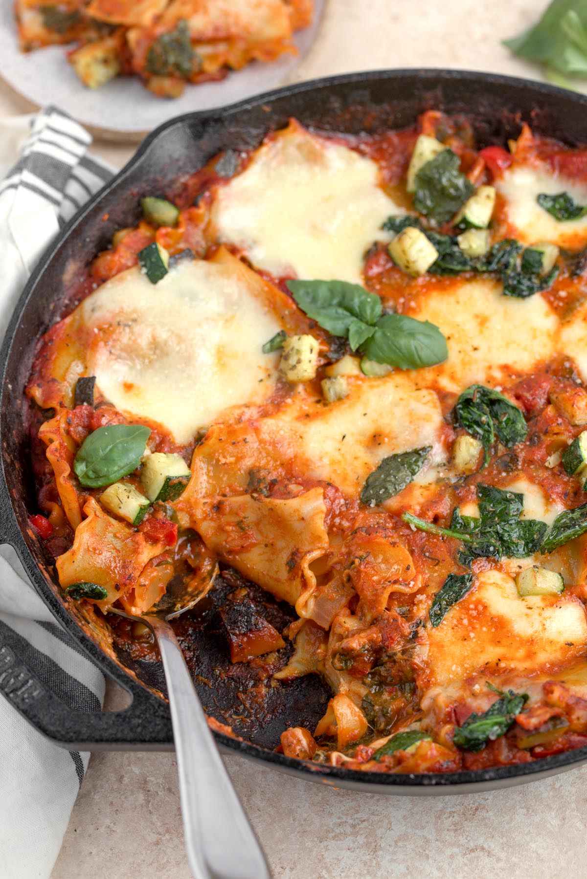A spoon scooping vegetable lasagna skillet out of a cast iron skillet