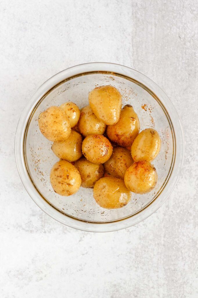Potatoes tossed in olive oil and seasoning in a mixing bowl.