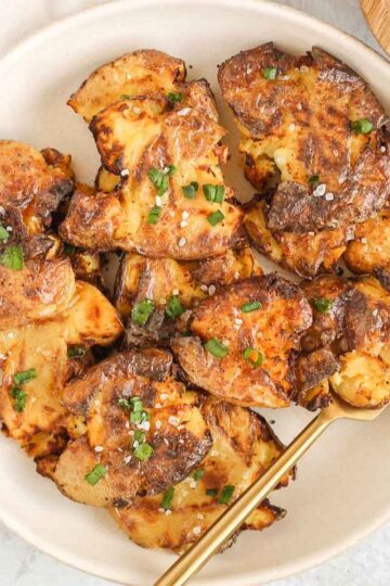 Fried smashed potatoes on a round serving plate with a gold fork.