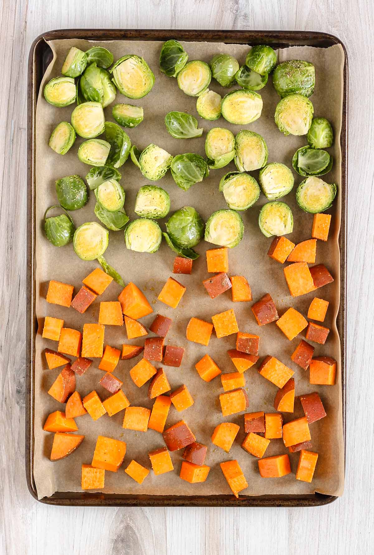 Raw Brussels sprouts and cubed sweet potatoes on a baking sheet.