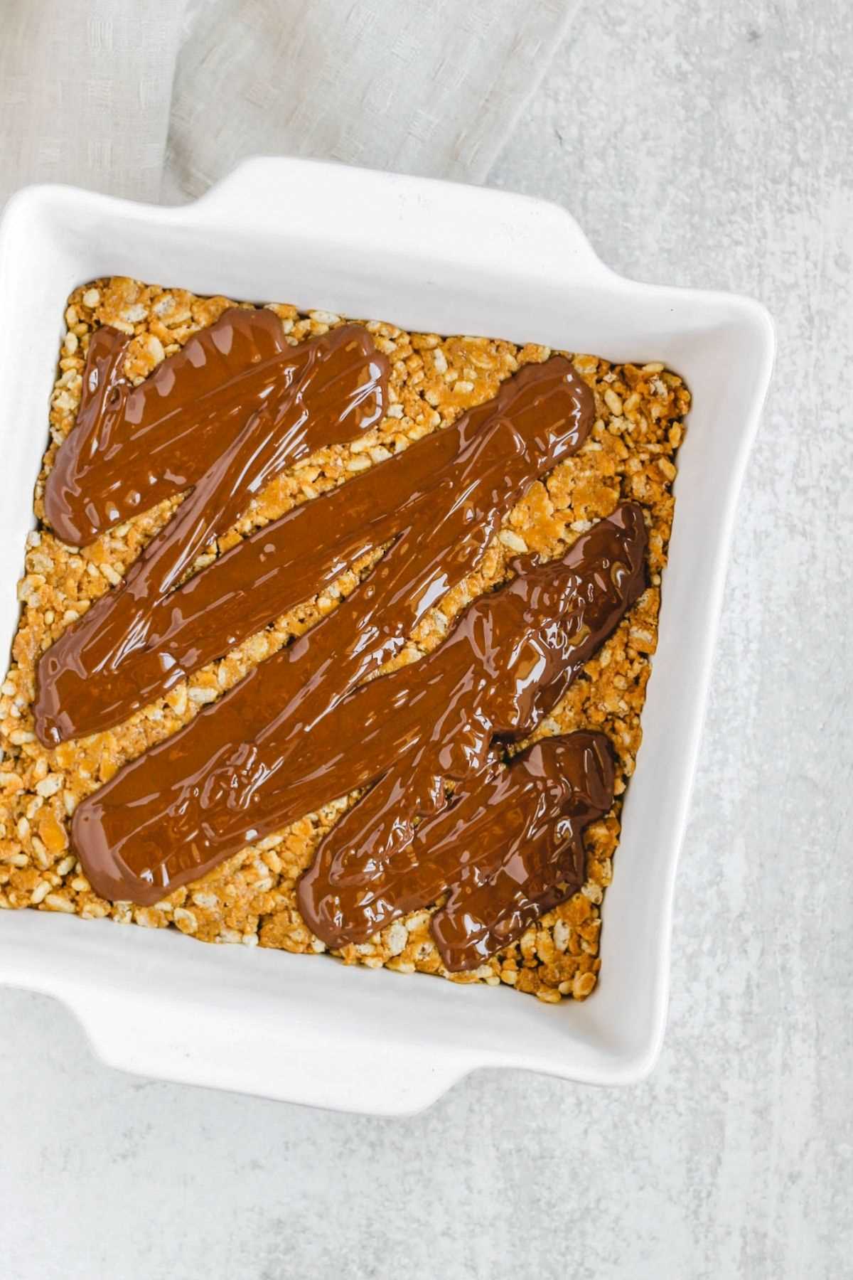 Peanut butter crispy bars in a square dish with chocolate drizzled on top.