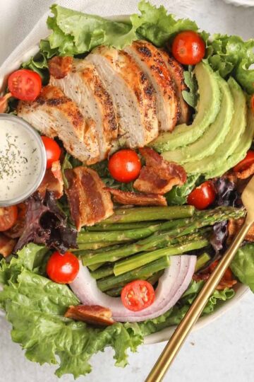 Salad bowl filled with a BLT salad with chicken, avocado, asparagus, and a side of ranch.