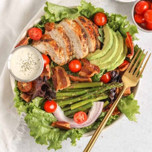 Salad bowl filled with a BLT salad with chicken, avocado, asparagus, and a side of ranch.