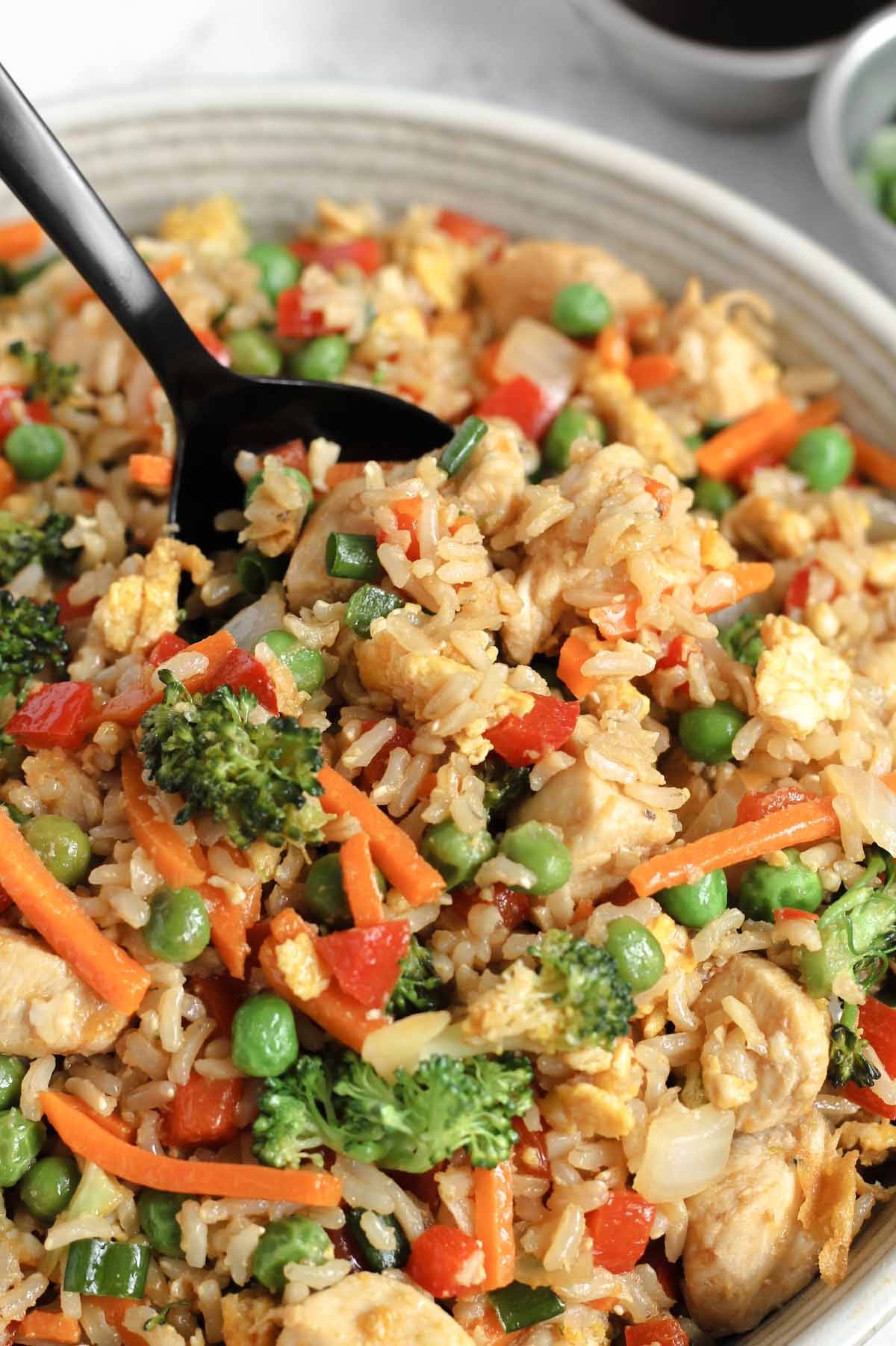Close-up of a spoon scooping healthy fried rice from a serving bowl.