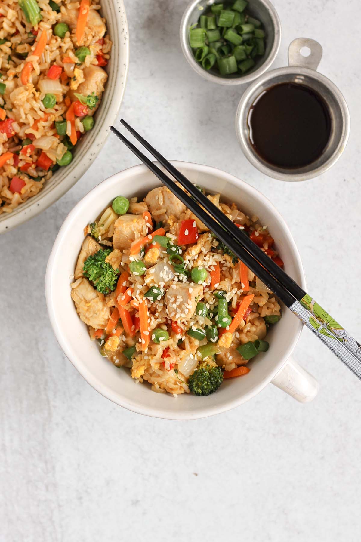 Chicken fried rice with lots of veggies in a single serve dish with chopsticks laid on top.