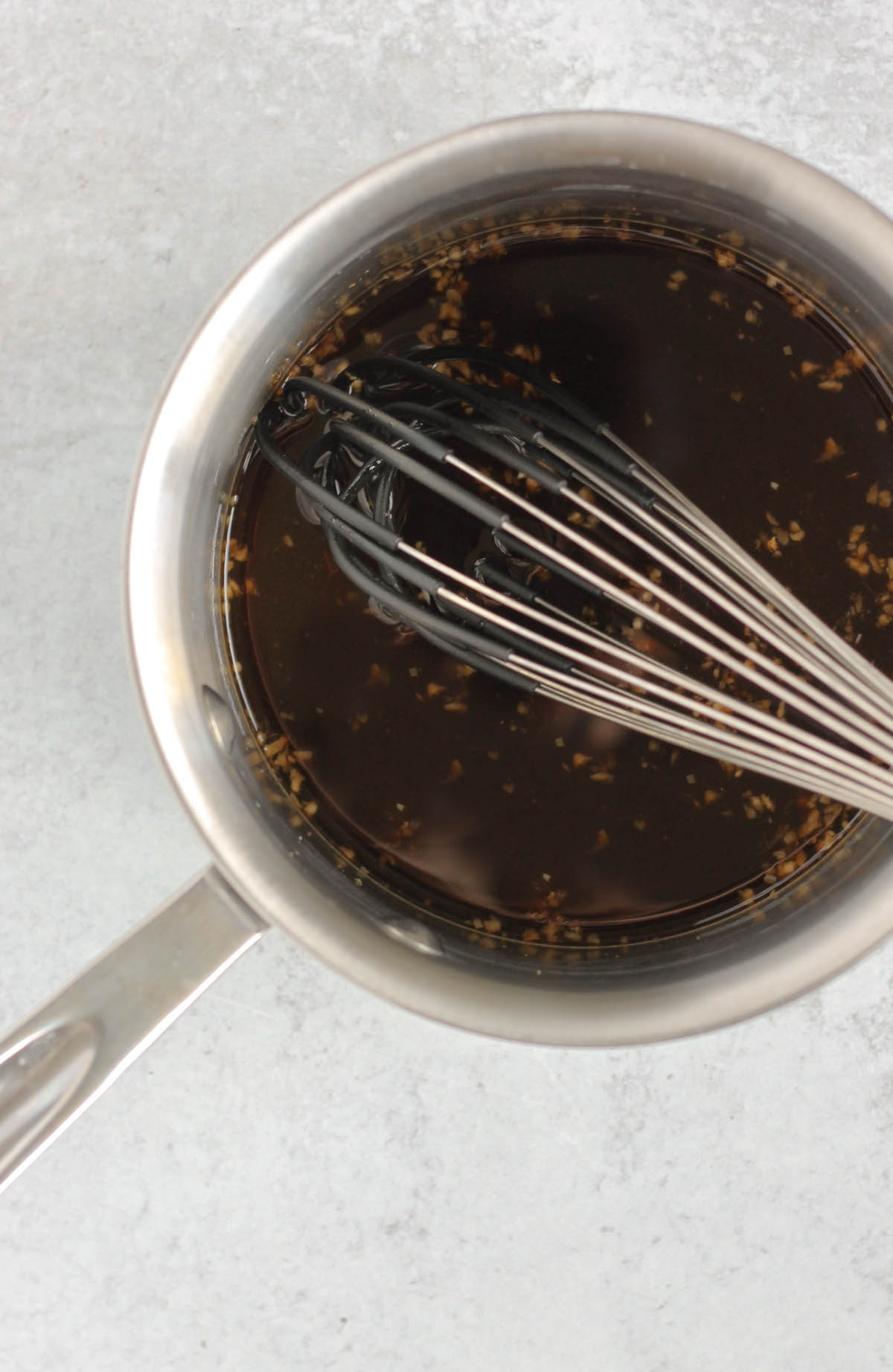 A whisk in a sauce pan filled with teriyaki sauce ingredients.