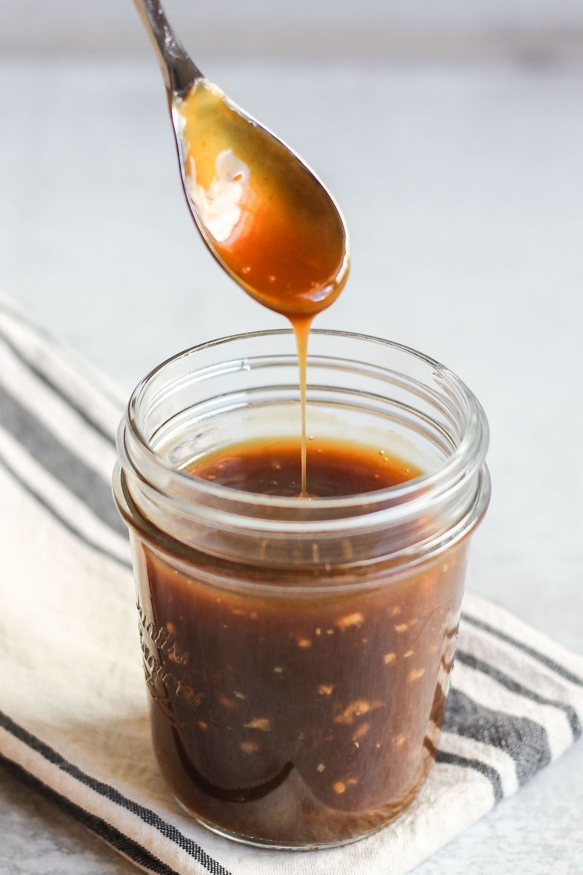 Teriyaki sauce dripping from a spoon over a mason jar filled with teriya