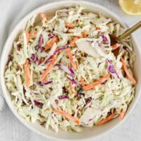 Creamy coleslaw in a serving bowl with a gold spoon.