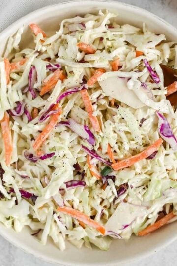 Creamy coleslaw in a serving bowl with a gold spoon.