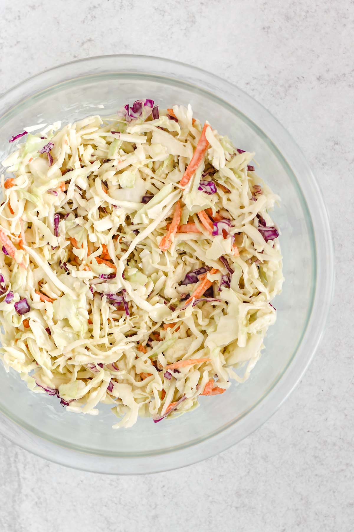 Coleslaw mixed with dressing in a mixing bowl.