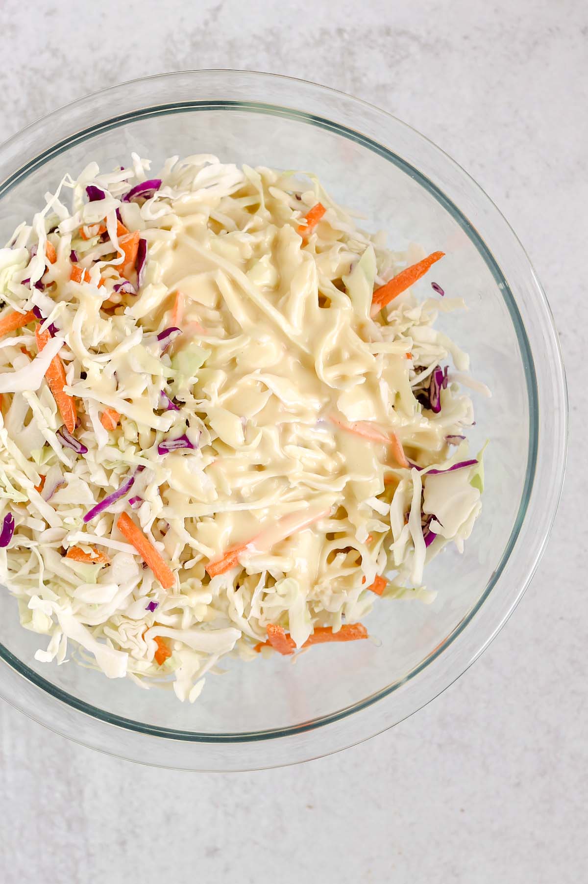 Dressing poured on coleslaw mix in a mixing bowl.