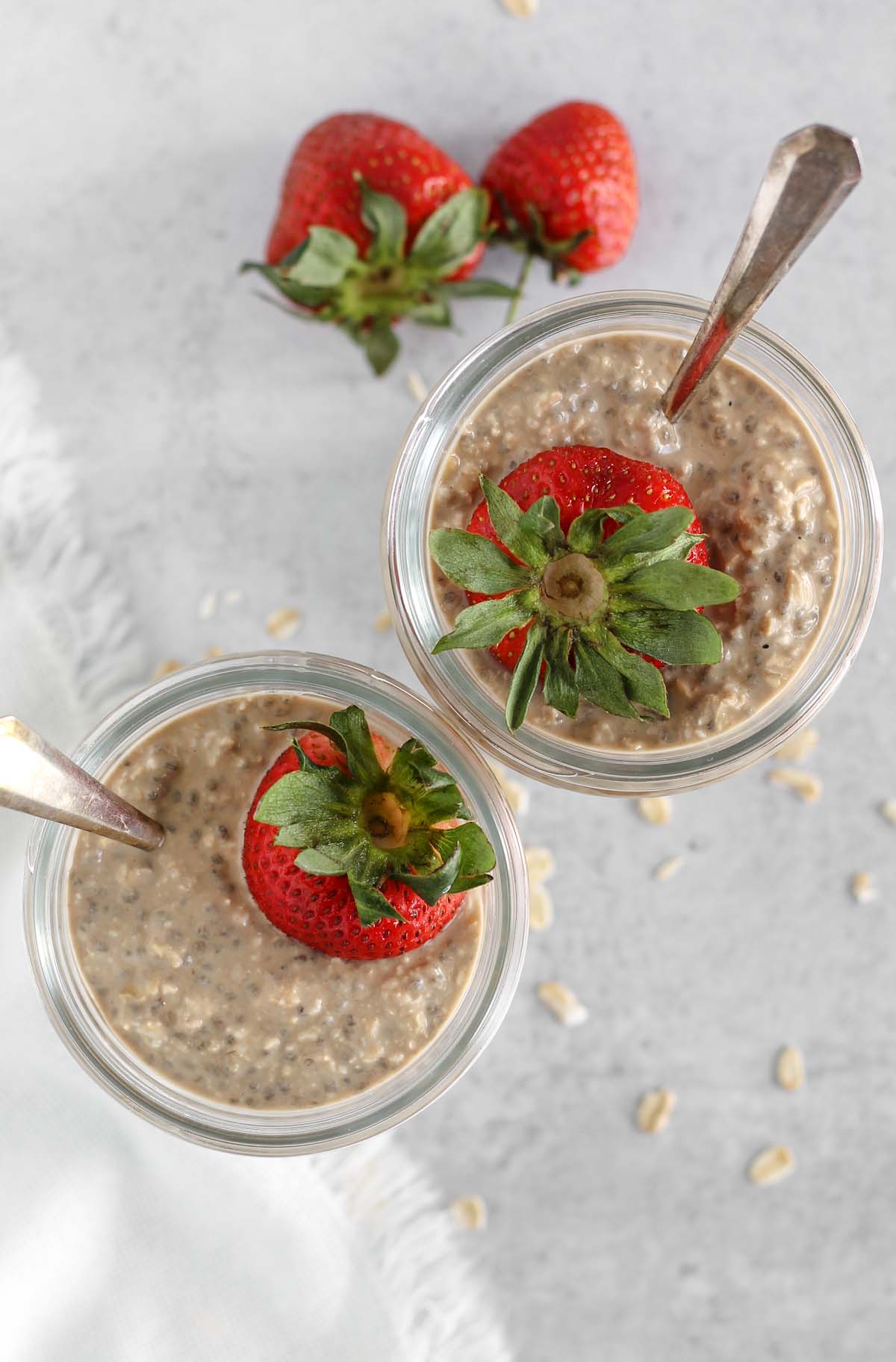 Overhead view of overnight oats topped with a strawberry in 2 mason jars.