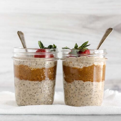 Two mason jars filled with overnight oats and almond butter topped with a strawberry.