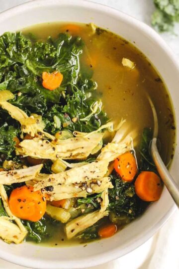 Chicken and kale soup in a white soup bowl with a spoon.